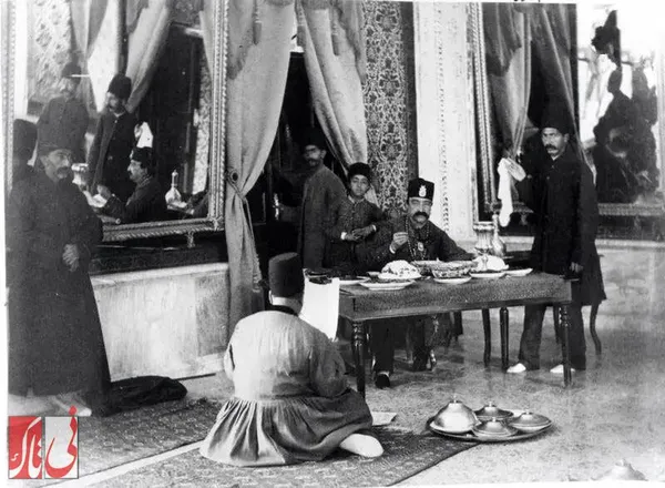 ناصرالدین شاه در حال صرف ناهار در کاخ گلستان و گوش دادن به مطالب یکی از درباریان که به حضور رسیده است
